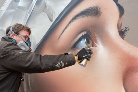 Mister Copy arbeitet mit Atemschutzmaske an einem Detail des Murals.