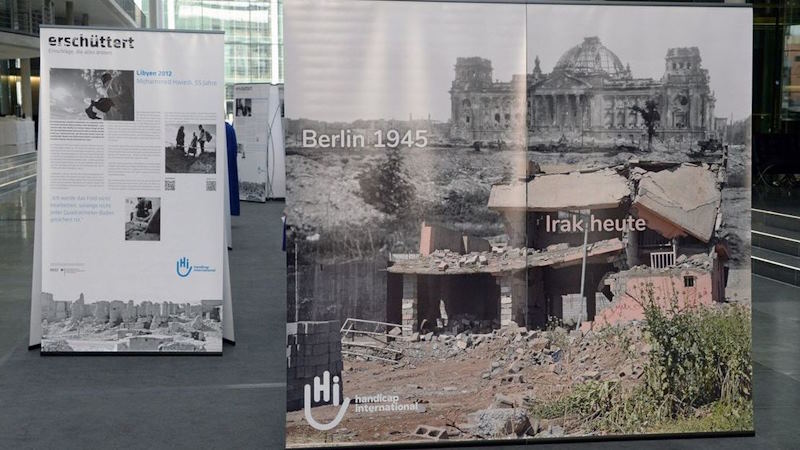 Ein Ausstellungsplakat zeigt zerbombte Städte im 2. Weltkrieg und im heutigen Irak