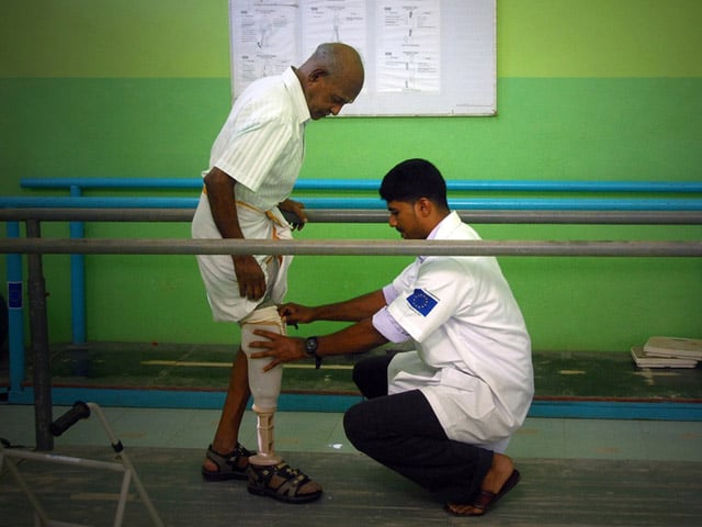 Ein Mann steht zwischen zwei Stangen zur Gehhilfe und ihm wird eine Prothese angepasst - HI Sri Lanka