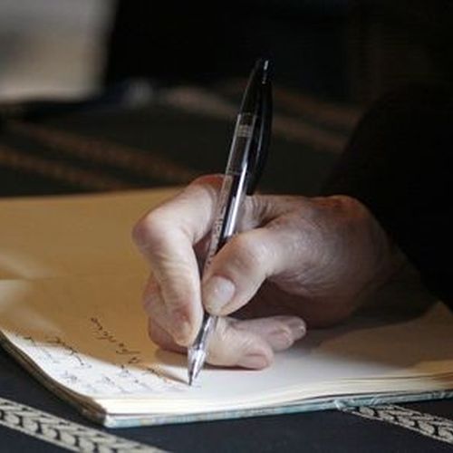 Hand einer älteren Person, die in ein Notizheft schreibt.