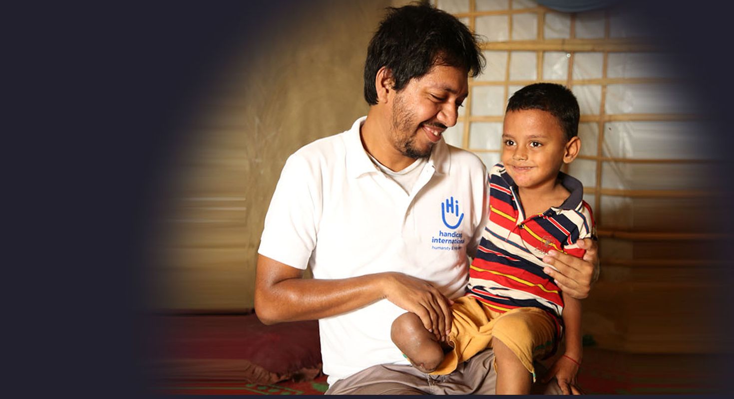 Ein Junge aus Bangladesch bei der Reha mit einem HI Mitarbeiter. Beide lächeln.