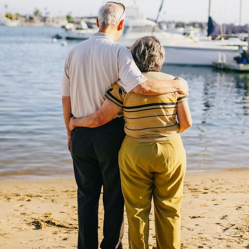 Älteres Paar steht mit dem Rücken zur Kamera an einem Hafen.