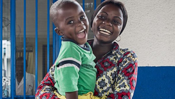 Eine afrikanische Mutter hält ihren Sohn auf dem Arm. Er trägt an beiden Beinen Orthesen. Beide strahlen übers ganze Gesicht.