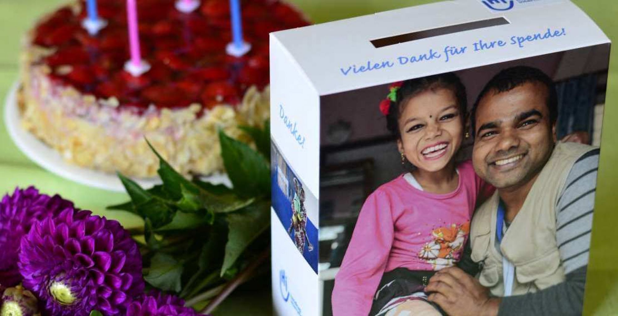 Ein gedeckter Tisch, auf ihm steht eine Spendenbox, ein Geburtstagskuchen und ein Blumenstrauß