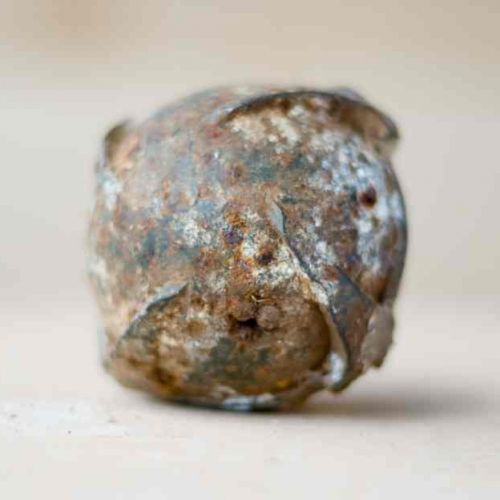 Eine einzelne Streubombe, sie sieht aus wie ein unregelmäßiger Ball aus Metall.