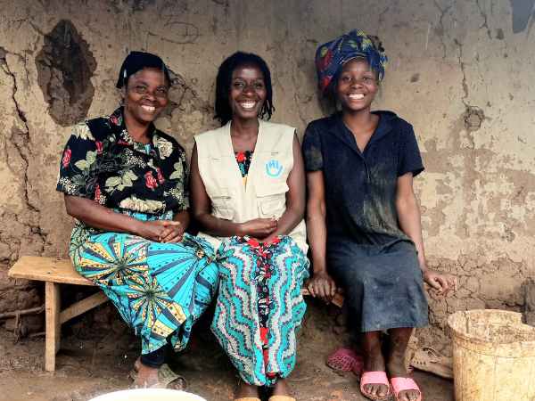 Drei Frauen sitzen vor einer Hütte in Uganda und lächeln in die Kamera. 