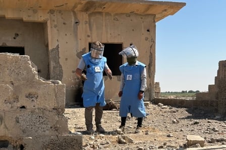 Ein Entminer in Ausrüstung kniet auf einer Wiese