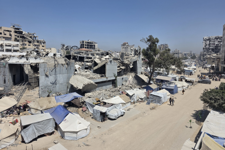 Ein kleiner Junge auf Krücken steht zwischen drei Mitarbeitenden von HI in einem Flüchtlingslager in Gaza.
